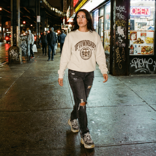 Two women posing on urban street wearing Uptownbaby graphic crewneck sweatshirts, one in lavender and one in black