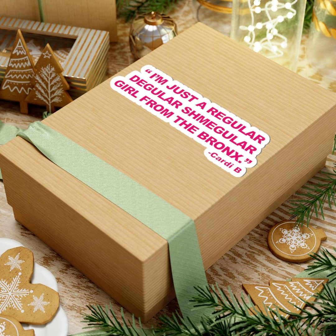 Cardi B quote sticker on gift box: 'I'm just a regular degular shmegular girl from the Bronx.' Holiday decor around.