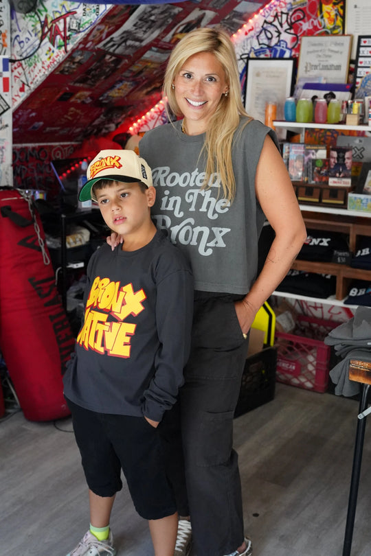 Two people posing together in a room with various items on shelves and a bed.