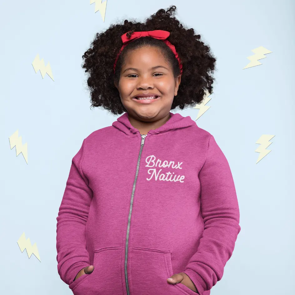 Child wearing a pink hoodie with 'Bronx Native' text on a light blue background
