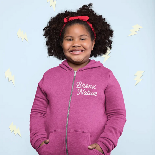 Child wearing a pink hoodie with 'Bronx Native' text on a light blue background