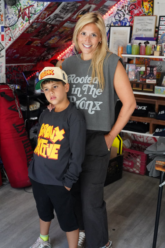 Two people posing together in a room with various items on shelves and a bed.