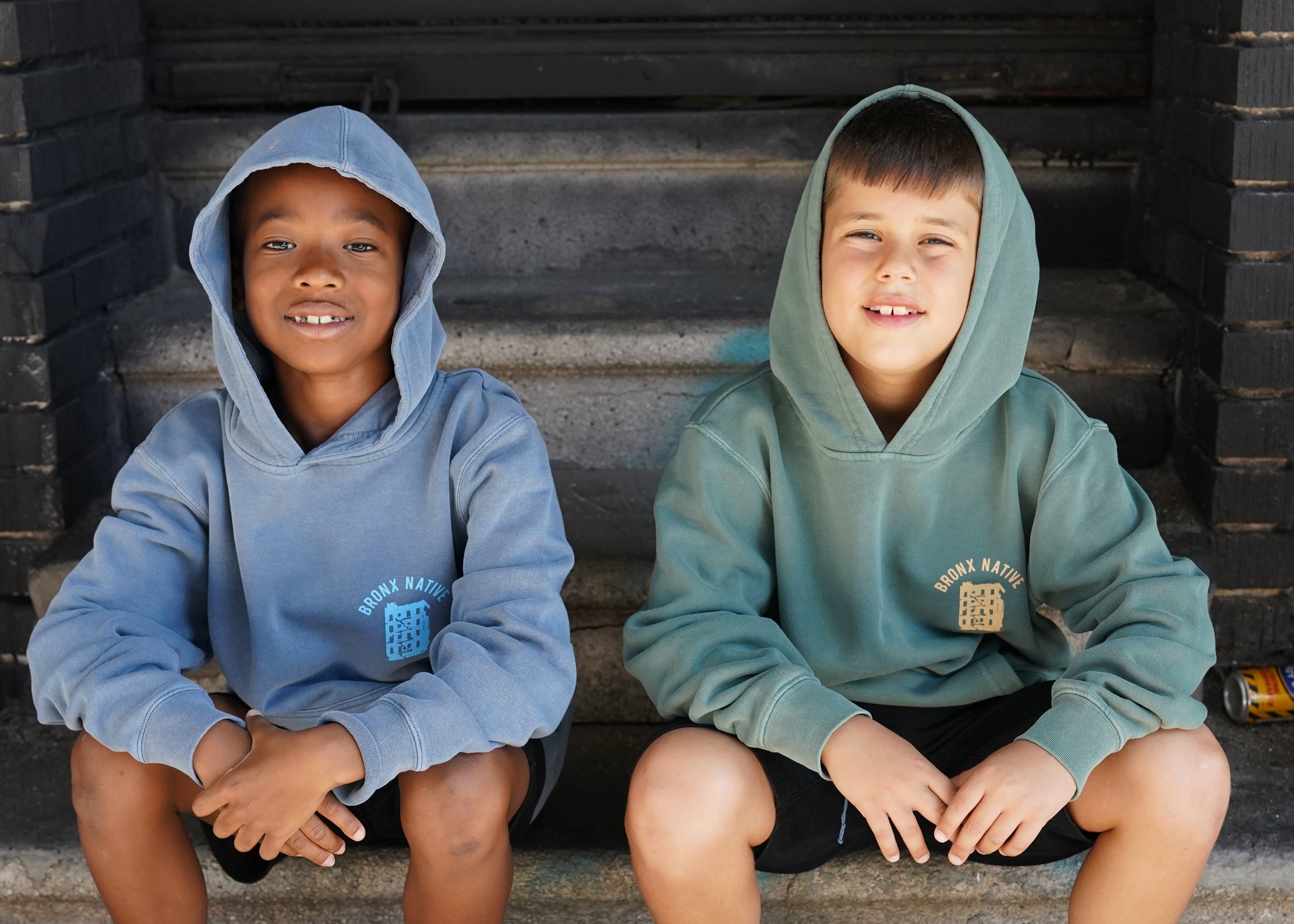 Two children wearing hoodies standing on a set of stairs.