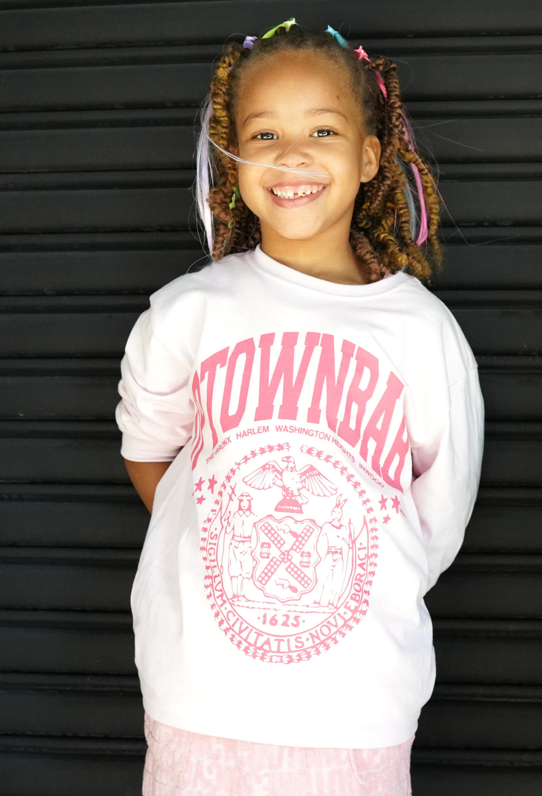 Young girl wearing a white sweatshirt with pink text and graphics against a black background