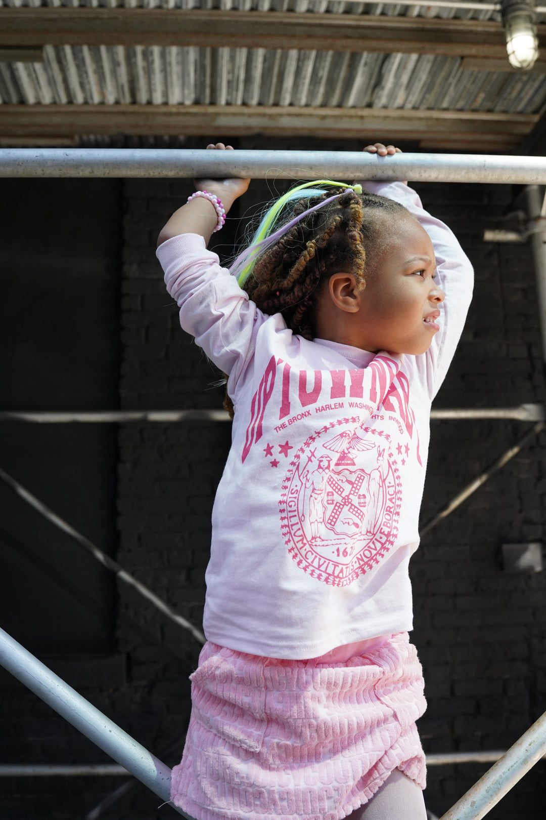Child in a pink and white outfit stretching on a metal structure