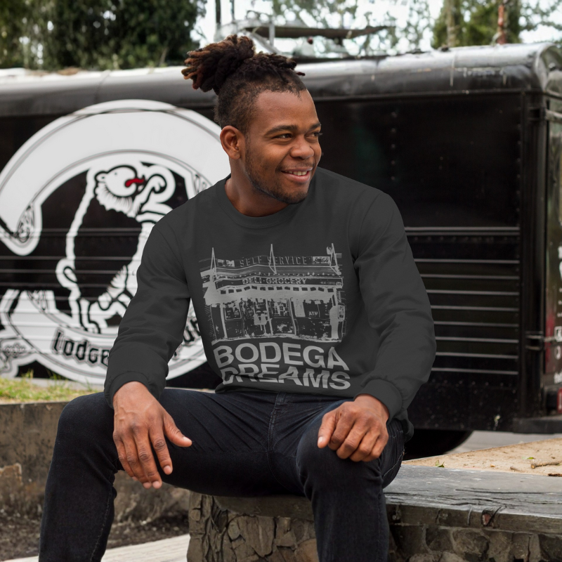 Man wearing a black sweatshirt with 'Bodega Dreams' text sitting in front of a vintage truck.